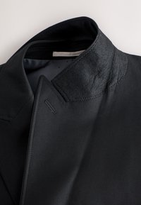 Fekete blézer gallér, texturált, filcszerű felülettel. Éles hajtókákkal és sima belső béléssel rendelkezik. Látható a művészi kidolgozás részletei.