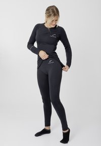 Zwarte thermische longsleeve top en aansluitende legging van rekbaar materiaal, met een subtiele logo op de borst en de tailleband.