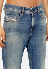 Vaqueros de denim azul con un lavado desgastado, detalles desgastados y un diseño de cinco bolsillos. Presenta un cierre de botón y sutiles acentos de costura.