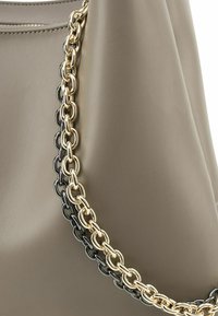 Beige leren handtas met een gestructureerd oppervlak en een gouden en zwarte schakelkettink met schakelriem die een contrasterend detail toevoegt.