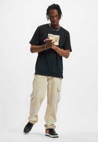 Sort bomulds T-shirt med grafisk print, parret med løse beige cargo bukser med sidelommer, afsluttet med sorte sneakers.