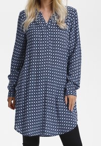 Niebieska i jasnoniebieska tunika w wzory z długimi rękawami, kołnierzykiem i plisą na guziki; charakteryzuje się diamentowym wzorem na miękkim materiale.