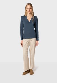 V-kauluksen pitkähihaisessa neuleessa tummansininen väri, pehmeä kangas, yhdistetty vaaleanbeigeihin korkeavyötäröisiin housuihin ja ruskeisiin tennareihin.