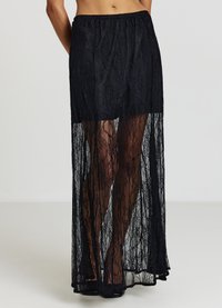 Jupe longue en dentelle noire avec un design transparent et une taille élastique. Le tissu présente un motif floral et descend jusqu'aux chevilles.