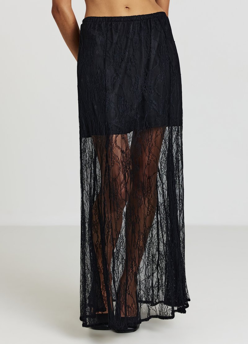 Jupe longue en dentelle noire avec un design transparent et une taille élastique. Le tissu présente un motif floral et descend jusqu'aux chevilles.