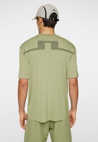 Vaaleanvihreä lyhythihainen paita, jossa on verkkokuvioinen yksityiskohta selässä. Yhdistetty vaaleanharmaaseen lippikseen, jossa on yksinkertainen logo.