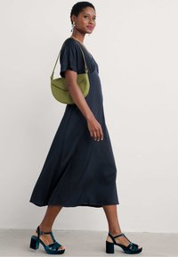 Merenmusta midi-mekko, jossa on lyhyet liehuvat hihat, yhdistettynä vihreään olkalaukkuun ja teal-sävyisiin platform-sandaaleihin. Sileä kangas ja virtaava muoto.