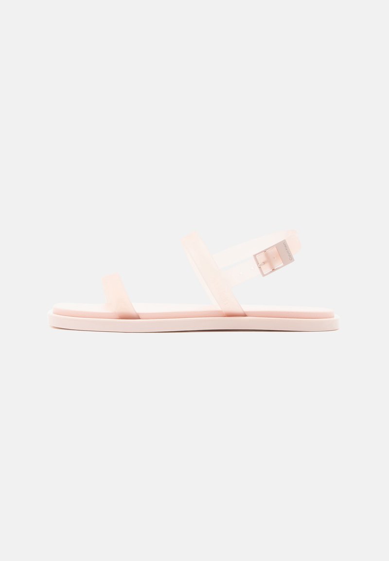 Sandale plate rose pâle avec deux fines lanières et une boucle ajustable sur la bride de cheville, vue de profil sur fond blanc.