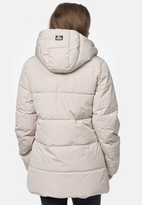 Doudoune beige clair avec capuche, présentant un design matelassé horizontal, une texture lisse et une petite étiquette de marque dans le dos.