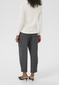 Valkoinen pitkähihaiseen paita yhdistettynä harmaisiin räätälöityihin housuihin. Paidassa on tiukka muotoilu, kun taas housut ovat löysät suoran leikkauksen omaavat. Mustat korolliset mules-kengät täydentävät asukokonaisuuden.