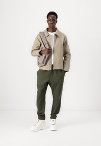 Light beige jacket, white t-shirt, and olive green pants. White chunky sneakers. Gray shoulder bag with a zipper. Simple design, casual fit.