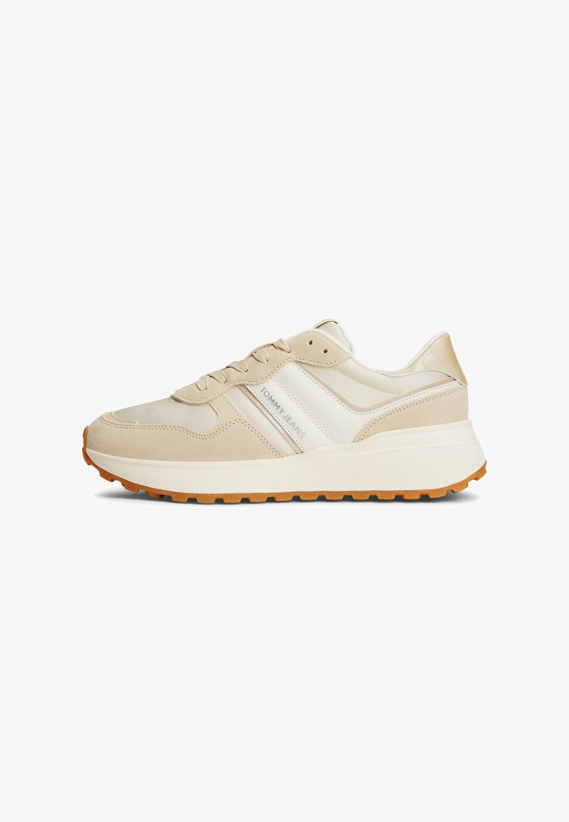 Zapatillas deportivas beige con parte superior de ante y malla, que presentan una franja lateral blanca y una suela de goma en color marrón claro.