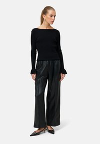 Czarny sweter z prążkowanego materiału o szerokim dekolcie, zestawiony z czarnymi spodniami z ekologicznej skóry o wysokim stanie. Czarne buty z detalami w postaci ćwieków.
