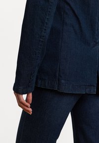 Donkerdenim jasje met een getailleerde snit, voorzien van een soepele textuur, vierknopen manchetten en een licht gebogen zoom.