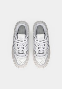 Par hvite og grå Adidas-sneakers med knyttede lisser, sett ovenfra på en enkel lys bakgrunn.