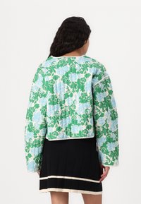 Prošívaná bunda s květinovým vzorem v zelené a modré barvě, s cropped designem a kontrastním lemem. Nositá přes černou plisovanou sukni.