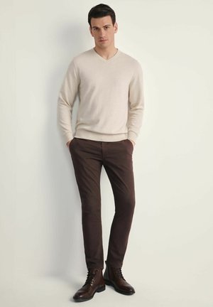 Beżowy sweter w serek, brązowe dopasowane spodnie i brązowe sznurowane botki; gładka faktura, proste linie i smukła sylwetka.