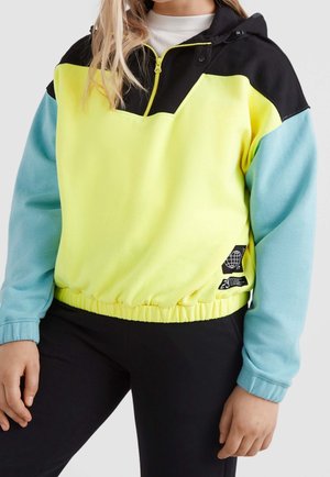 Person wearing a color-block pullover with black hood, yellow chest, light blue sleeves, and a small black patch on the waist.