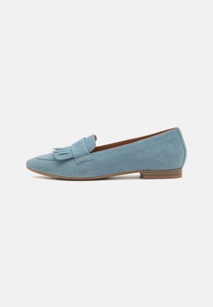Mocassin plat en daim bleu clair avec détail à franges et petit talon en bois empilé sur fond blanc.