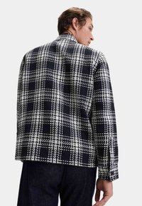 Czarna i biała, w kratkę, kurtka o fakturowanej tkaninie, z kołnierzem, zapinanymi mankietami oraz lekko oversize'owym krojem.