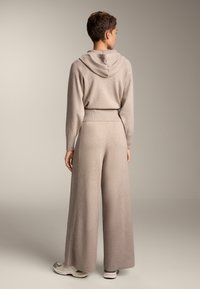 Beige stickad hoodie med ribbat avslut, tillsammans med vida byxor. Mjuk textur, minimalistisk design och huva synlig.