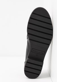 Semelle d’une botte noire avec larges rainures horizontales pour l’adhérence, taille 37, nom de la marque « Tamaris » embossé sur la semelle.