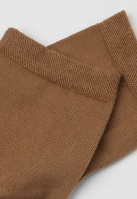 Calcetines de canalé marrones con una textura suave. Presenta una banda ancha y ajustada en la parte superior y un cuerpo liso, adecuados para un uso casual.
