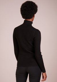 Schwarzer gerippter Rollkragenpullover mit langen Ärmeln und tailliertem Design. Aus strukturiertem Strickmaterial gefertigt, betont er eine schlanke Silhouette.