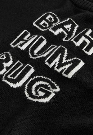Black knit sweater featuring bold white text that reads "BAH HUM BUG" in a mix of uppercase and stylized lettering. Textured fabric detail visible.