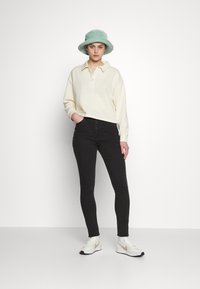Sweatshirt cropped, de cor creme, com colarinho, combinado com jeans ajustados pretos. Usado com um chapéu estilo balde verde claro e ténis brancos.