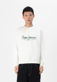 Sudadera blanca con texto verde "Pepe Jeans" en estilo cursiva, cuello redondo y mangas largas, combinada con pantalones cortos negros con costuras blancas.