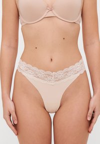 Naakte string met een bloemvormige kanten tailleband, gemaakt van soepele materialen en met minimale bedekking, ontworpen met een zachte textuur en nauwkeurige afwerking.