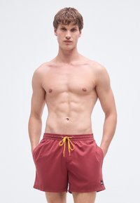 Punased ujumispüksid kummipaela ja kollase nööriga. Varustatud küljetaskutega ja vasakul säärel väikese musta logoga.