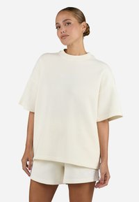 T-shirt oversize a coste crema con maniche corte e collo a giro, abbinato a pantaloni corti coordinati con un piccolo logo.