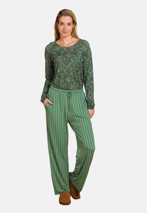 Groene top met lange mouwen en een bloemmotief, gecombineerd met groene gestreepte wijde broek. Model draagt bruine schoenen. Casual loungewear.