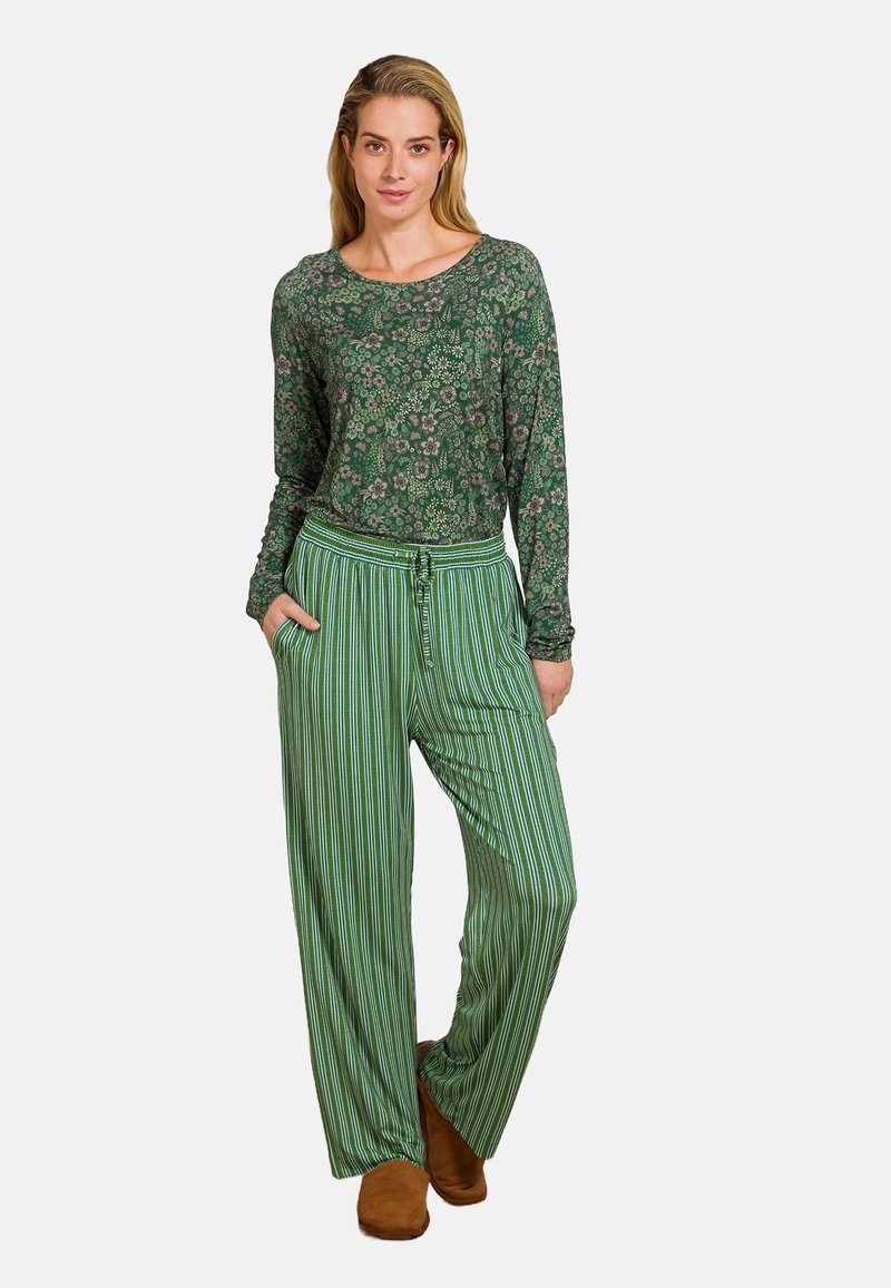 Groene top met lange mouwen en een bloemmotief, gecombineerd met groene gestreepte wijde broek. Model draagt bruine schoenen. Casual loungewear.