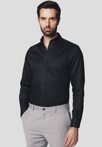Czarna koszula z guzikami, z klasycznym kołnierzykiem i długimi rękawami, w połączeniu z jasnoszarymi spodniami. Gładka tekstura z delikatnym połyskiem.