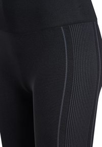 Schwarze Sportleggings mit gerippter Textur und dezenten seitlichen Einsätzen, die vertikale Streifen und ein figurbetontes Design aufweisen.