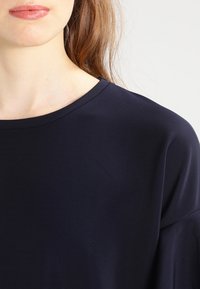 Marineblaues T-Shirt mit Rundhalsausschnitt, glatter Textur und kurzen Ärmeln, mit lockerer Passform und dezenten Rippdetails am Ausschnitt.