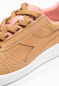 Světlé semišové tenisky s hladkým koženým akcentem, perforovan ými detaily a tkanými šňůrkami, s bílou gumovou podrážkou a růžovým vnitřním podšíváním.