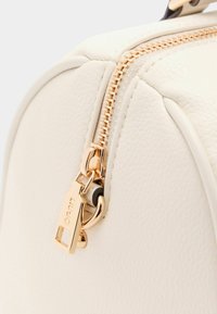 Coin de sac en cuir crème avec une finition texturée, doté d'une fermeture éclair dorée et de détails en métal, mettant en avant la durabilité et le design.