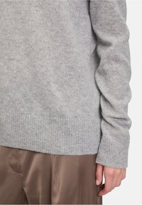 Szürke kasmír pulóver bordás mandzsettákkal és szegélyezéssel, puha, sima textúrával és laza szabással, barna selyem nadrággal párosítva.