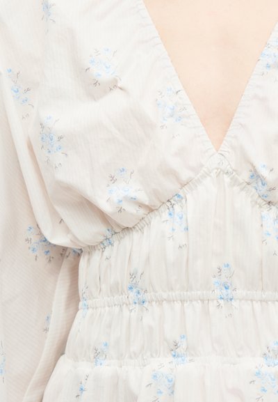 Κοντινό πλάνο λευκού υφάσματος με μικρά μπλε ανθισμένα σχέδια και ελαστικό ρέλι στη μέση, με βαθιά V λαιμόκοψη.
