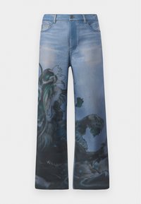 Leve hoitavat farkut vaalennetusta sinisestä denimestä, jossa on monimutkainen graafinen kuvio, joka sisältää yksityiskohtaisen mustan ja turkoosin sävyisen suunnittelun yhdellä jalalla.