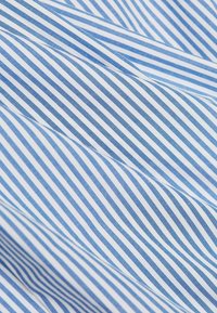 Gros plan d'un tissu bleu et blanc avec des fines rayures diagonales et des plis visibles créant des vagues douces.