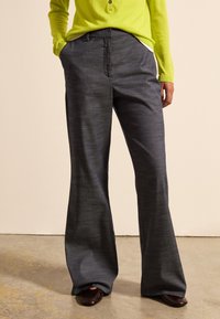 Graue, ausgestellte Hose aus strukturiertem Stoff, mit einem normalen Bund und seitlichen Taschen, kombiniert mit einem leuchtend grünen Langarmoberteil.