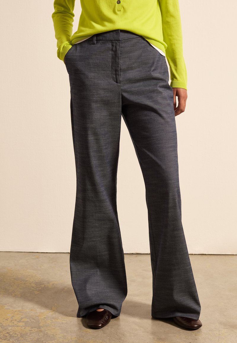 Graue, ausgestellte Hose aus strukturiertem Stoff, mit einem normalen Bund und seitlichen Taschen, kombiniert mit einem leuchtend grünen Langarmoberteil.