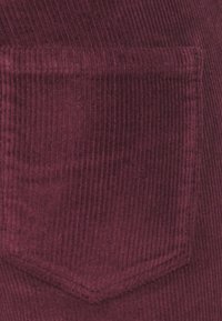 Burgundy corduroy fabric pocket with vertical ribbing, featuring a pointed shape and neat stitching along the edges.