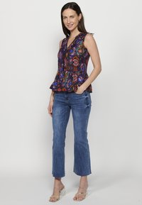 Ujjatlan peplum top, amely színes, díszes mintával rendelkezik sötét háttéren, világoskék trapéznadrággal és átlátszó sarkú szandálokkal párosítva.