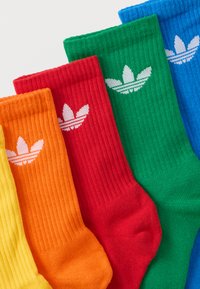 Öt színes, bordázott zokni sárga, narancssárga, piros, zöld és kék színekben, mindegyiken egy fehér Adidas trefoil logó található a szegély közelében.